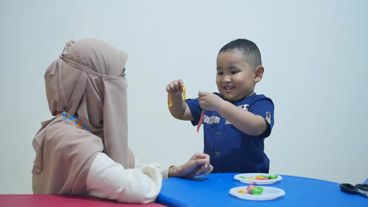 Guru berbincang dengan anak di meja kelas